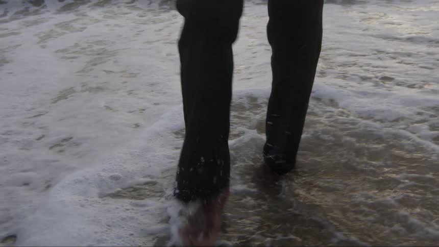Man carries smiling woman as he wades through water on the beach
