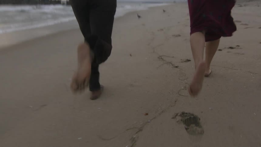 Young couple running barefoot on the wet sand beach next to the ocean