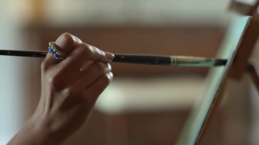 Close up of the hand of a woman painting on a board with a brush