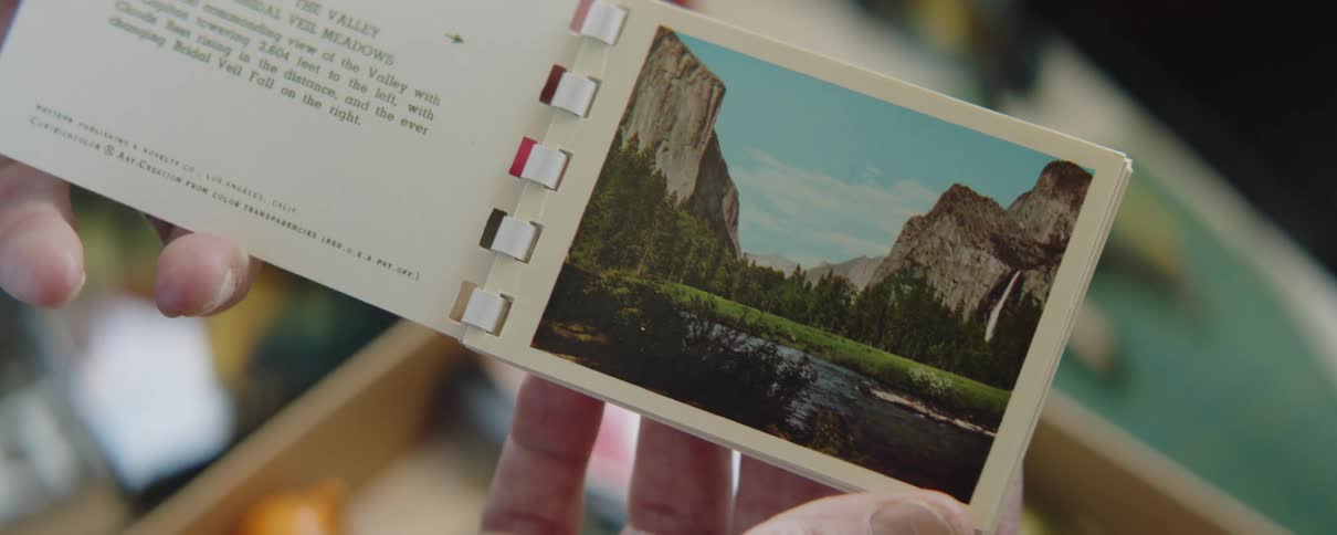 Person holds small booklet open to page showing a nature scene