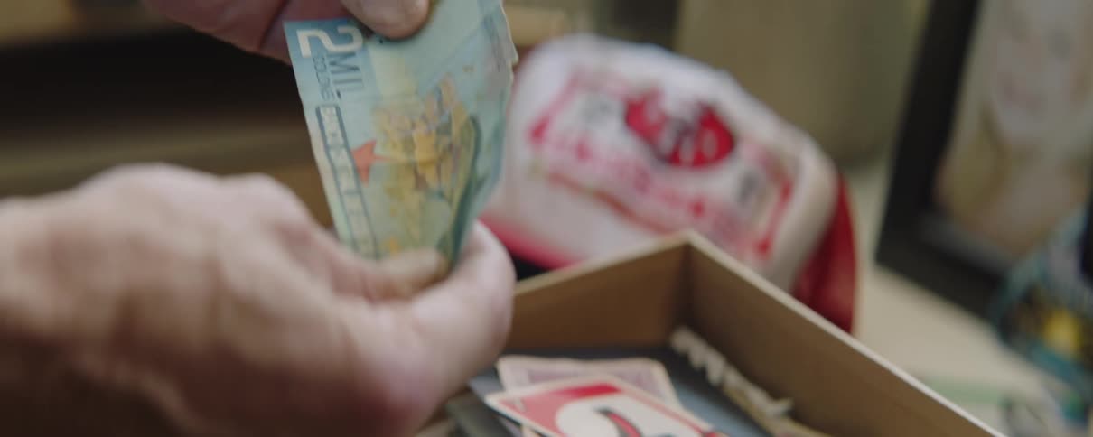 A man reaches into a box of notes and papers and takes a paper in his hands that appears to be foreign currency