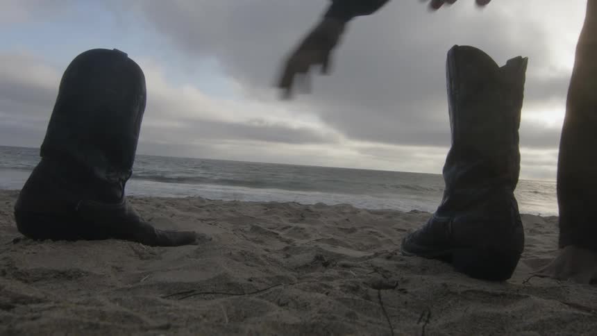 Young couple pick up their shoes from the sand beach next to the ocean at evening