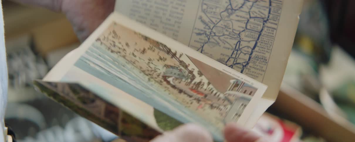 A man looks through a pile of postcards and reads one containing a map