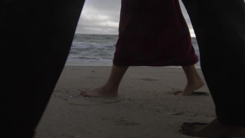 Young barefoot couple walking on the sand beach next to the ocean