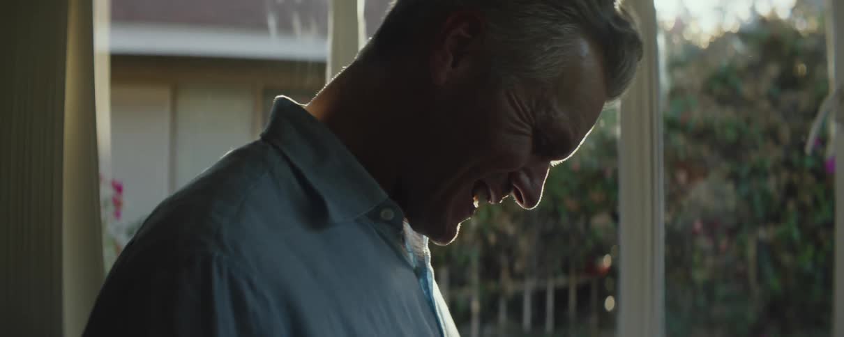 Sun shines behind a mature man standing in a room at home in the morning