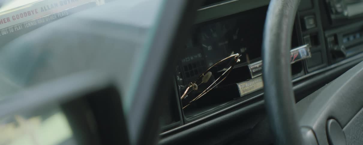 Inside of an automobile sunglasses and vhs tapes are sitting near the speedometer and steering wheel
