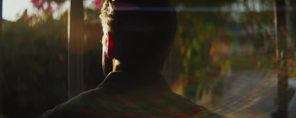 Sun shines behind a mature man standing in a room at home in the morning