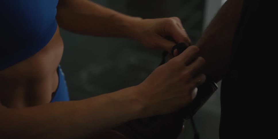 A woman is putting gloves on a man in a gym