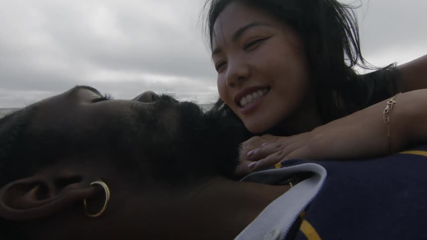 Woman lies against mans chest as he strokes her hair while they lie on the beach