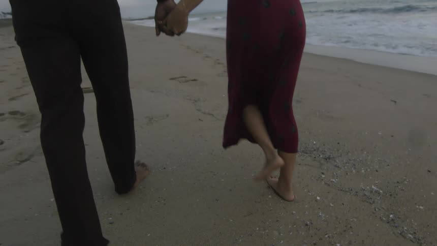 Man and woman walk across beach barefoot holding hands