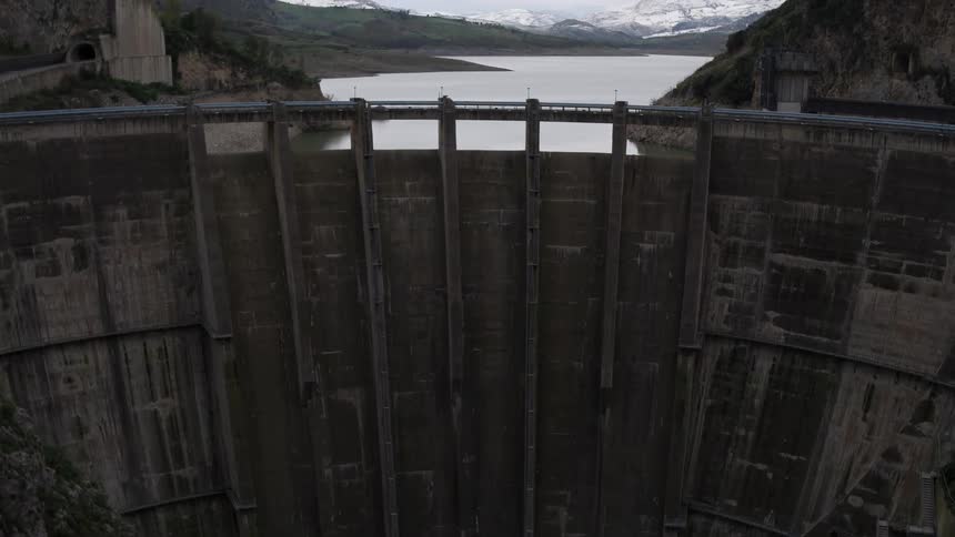 A tall dam holds back a water in a mountain region