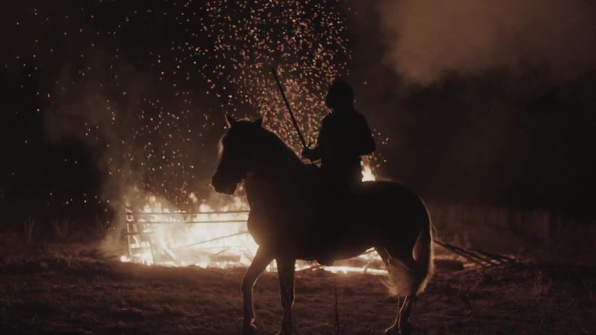 A man sits on a horse near a burning fence