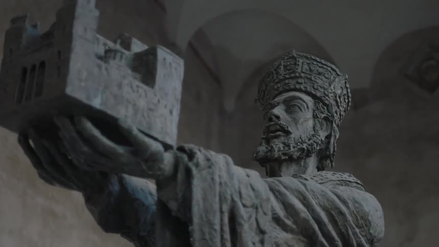 A statue of a man with a crown holding a building in his hands