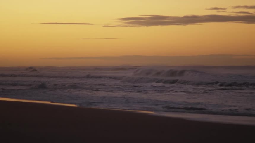 Waves foam as they roll onto beach under a red sky
