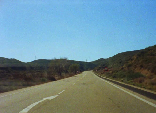 Driving on a lonely rural road next to the hills at daytime caught on vintage film