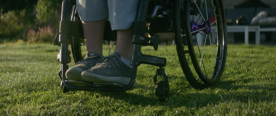 Woman on a wheelchair stops over the green lawn on the backyard at morning