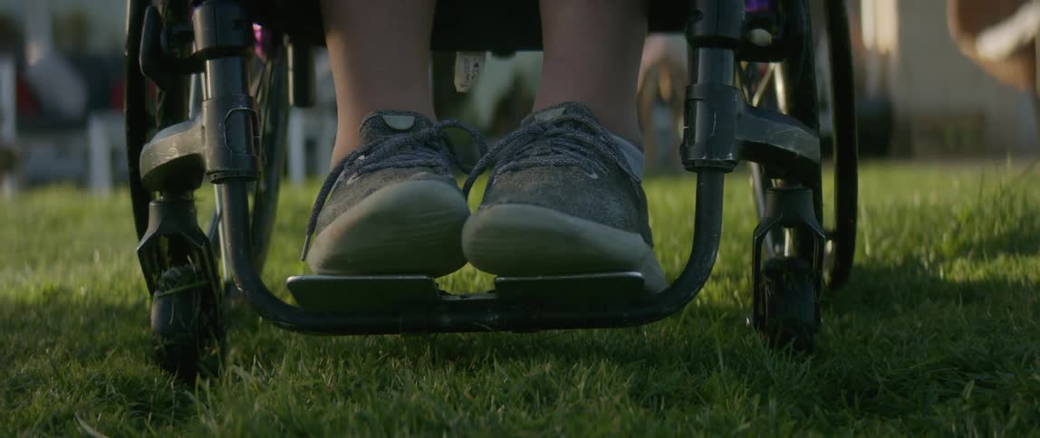 Female wheelchair user wearing a pair of gray shoes gets about on the lawn