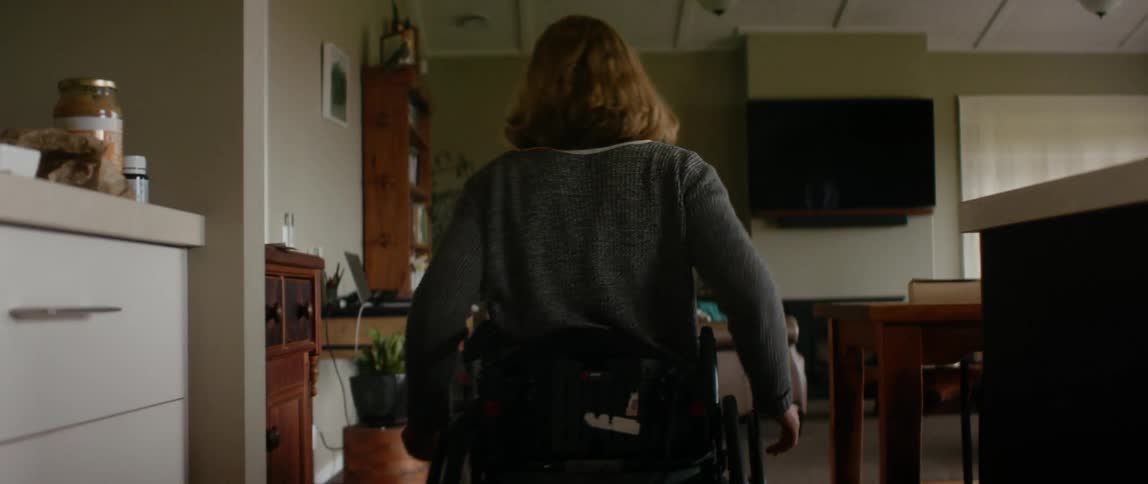 Young woman sitting on a wheelchair moves from the kitchen to the living room