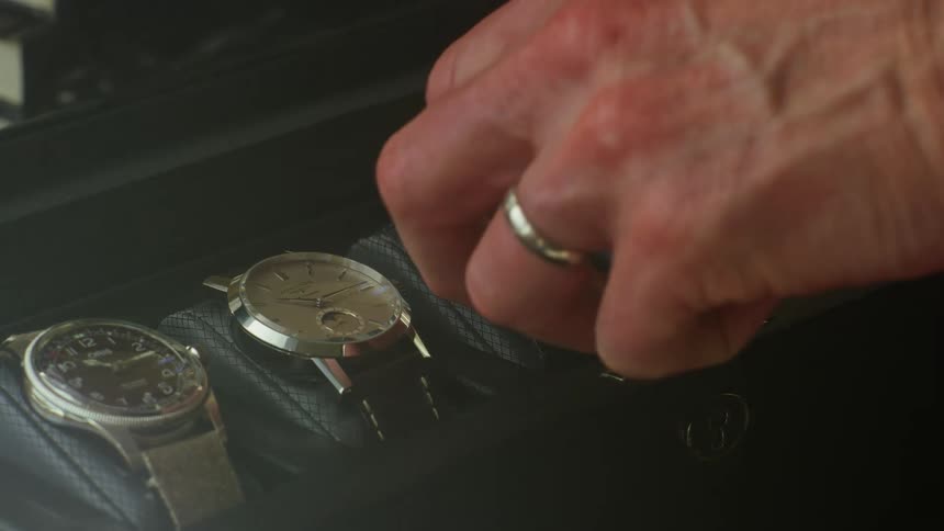 Five wristwatches are in a display case and a man takes the one in the middle