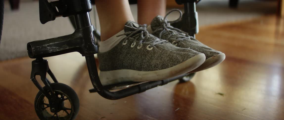 Woman in wheelchair puts on pants in living room at home