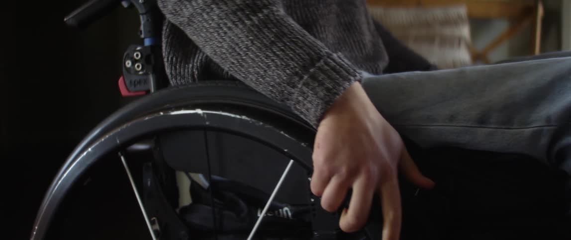 A girl in a wheelchair rolls into a room as she holds the wheels with her hands