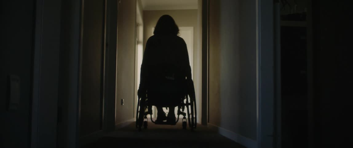 A woman wheels her wheelchair down a hallway in her home