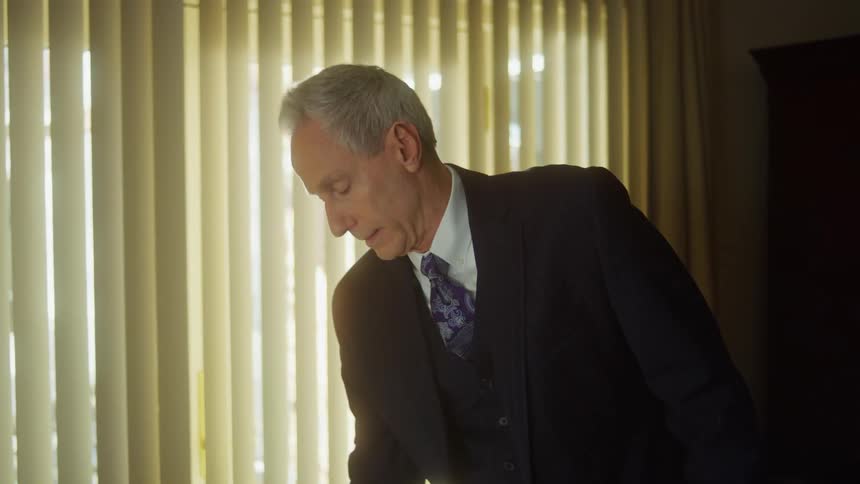 Older man wearing a suit finishes a phone call then looks at case with several wristwatches