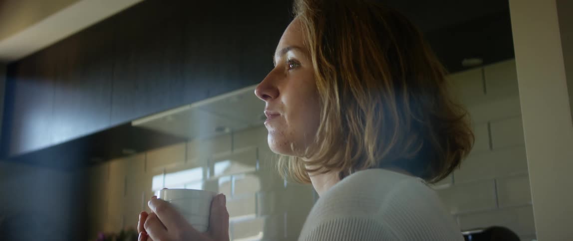 A woman is in her kitchen and drinking coffee