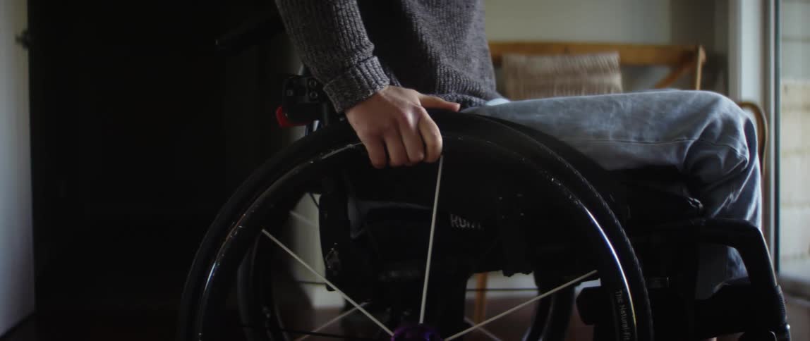 A girl in a wheelchair rolls down a hallway and into a room as she holds the wheels with her hands