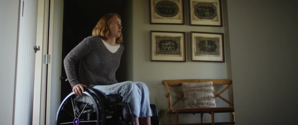 A girl in a wheelchair rolls into a room as she holds the wheels with her hands