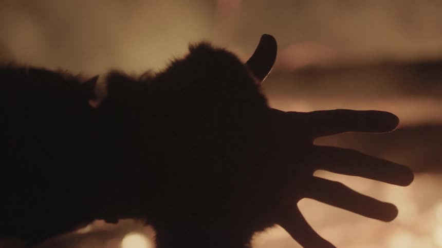 A man opening his fist and spreading his fingers out in front of a fire