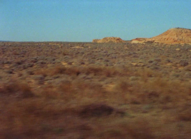 During road trip moves past scrub land and dirt hills under a cldar blue sky