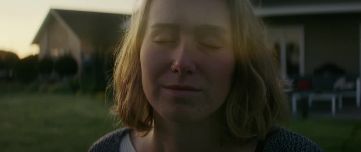 A woman outside her home smiles and closes her eyes