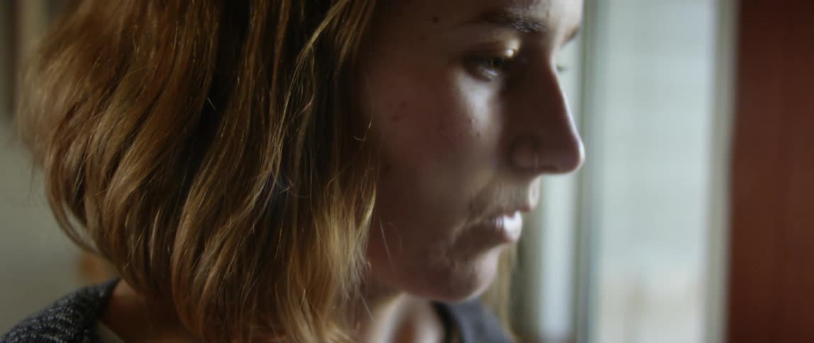 Light shines on a girls face as she is sitting inside a room looking down