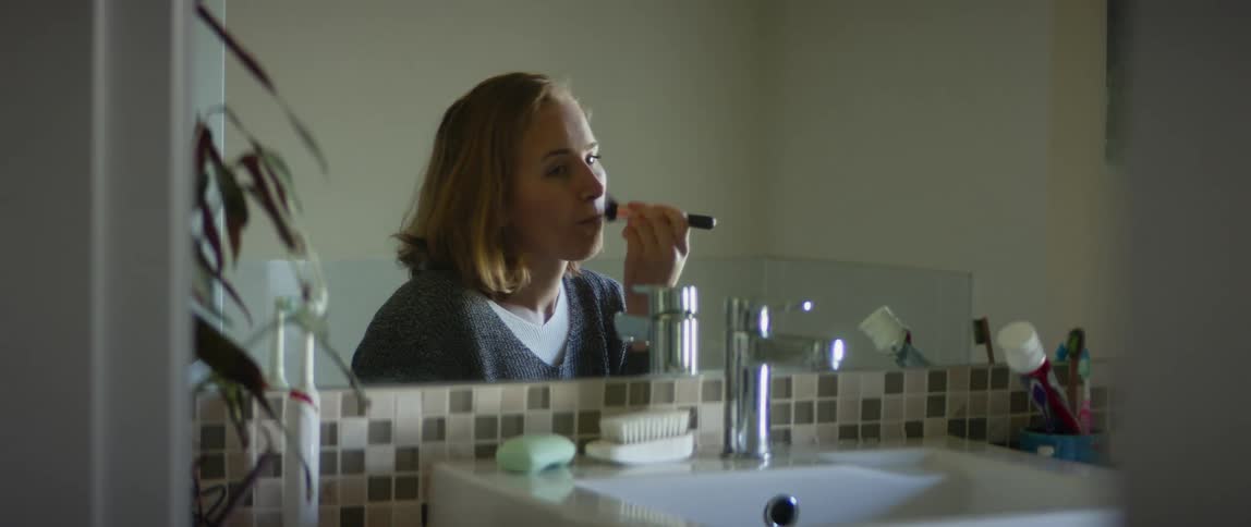 A woman sits in her bathroom and puts make up on