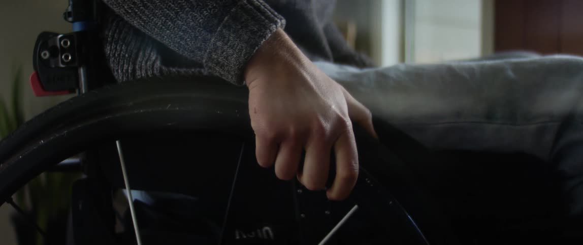 Person sitting in wheelchair grasps wheel and taps it with a finger