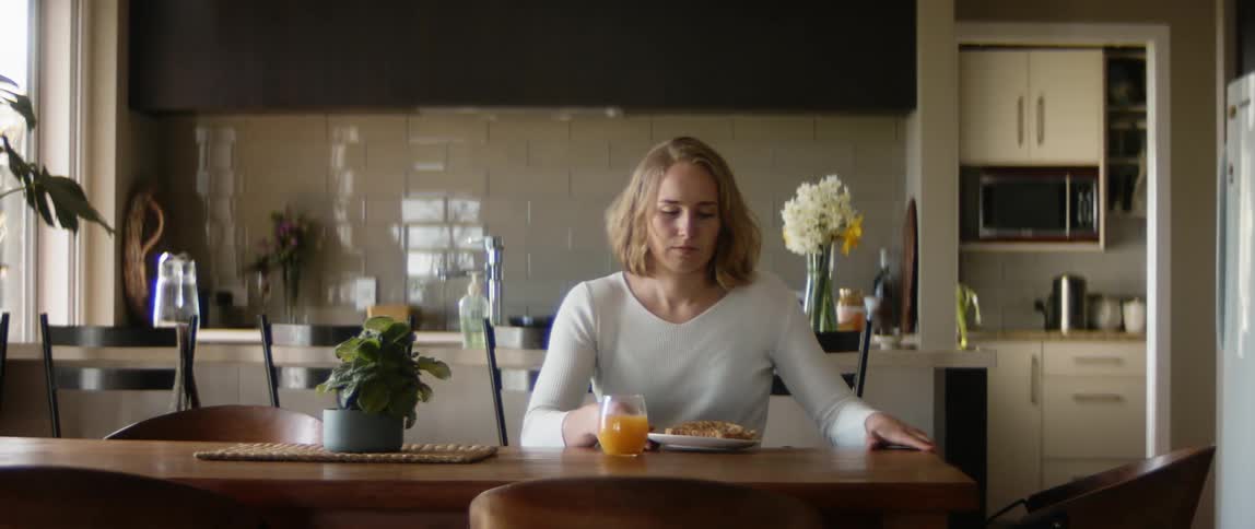 A woman in a wheelchair at home wheels herself to the table and sets down a plate with toast and starts to eat