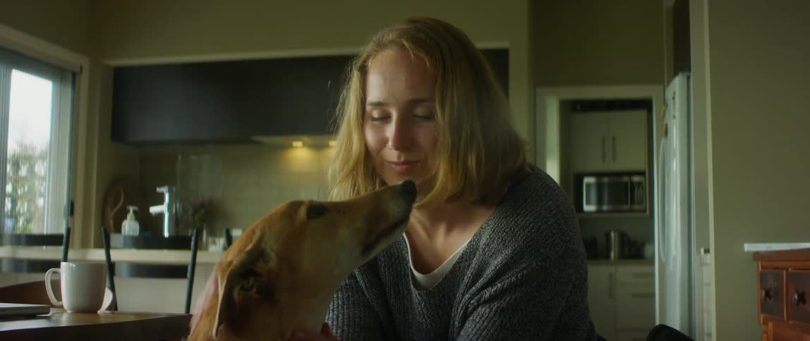 A woman sitting in a wheelchair at home pets her dog