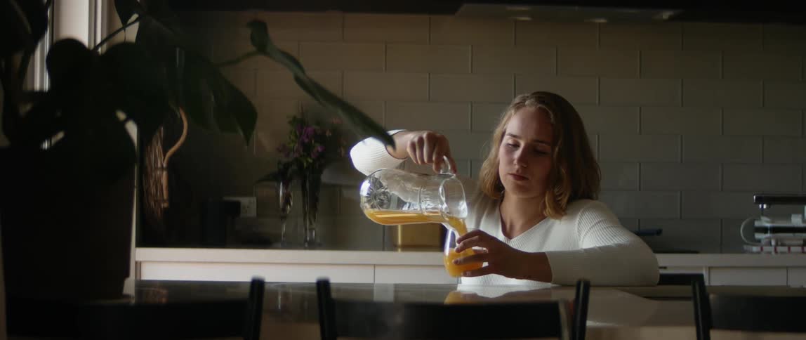 A woman is in her kitchen and drinking juice