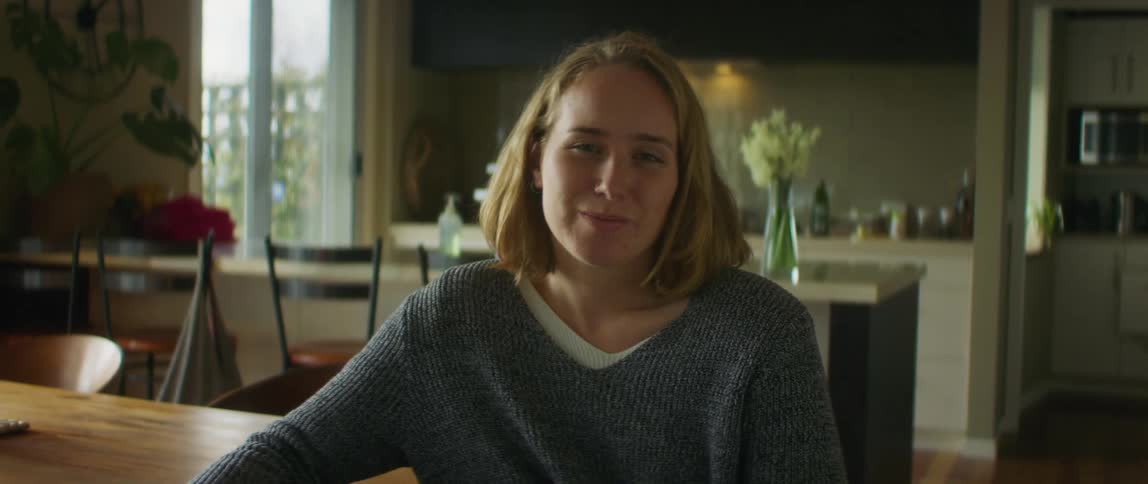 A teenage girl is sitting at the kitchen table with a smile on her face