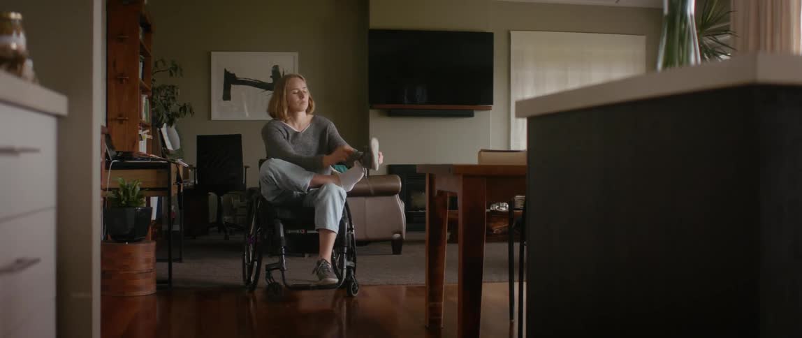 Blonde female wheelchair user puts on shoes in the living room
