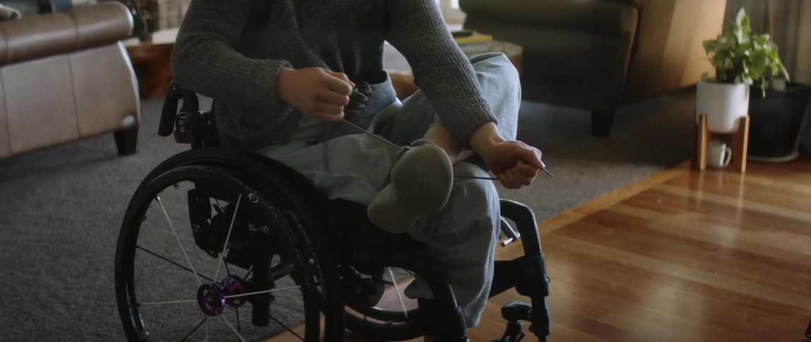 Young woman sitting on a wheelchair in the living room puts on shoes