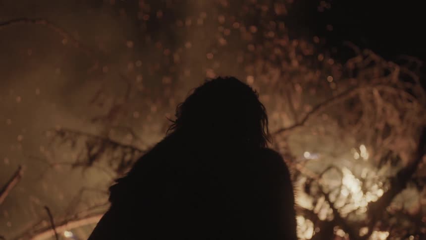 A man leans forward towards burning trees at night