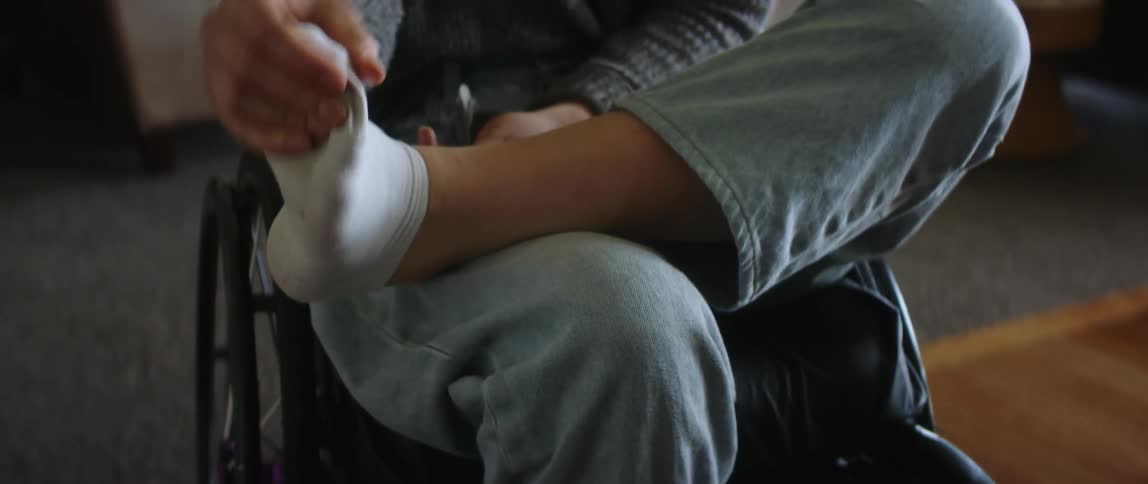 Woman sitting in a wheelchair in the living room massaging her foot