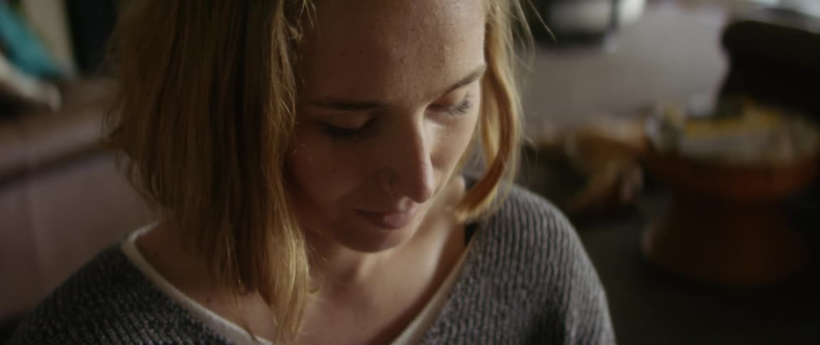 Blonde female wheelchair user wearing gray sweater looks down at smartphone smiling slightly