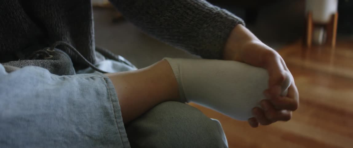 A person is sitting indoors and touching their foot