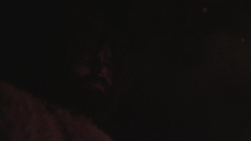 A bearded man stands in the shadows