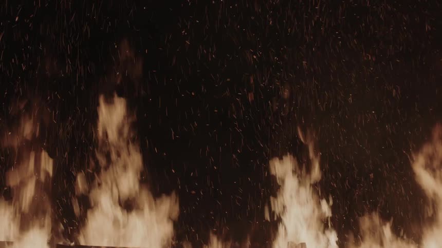 A fence-like structure made of wood slats is burning at night