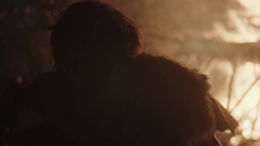 A man wearing furs is standing before a raging bonfire
