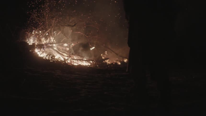 A man approaches a burning pile of branches and trees